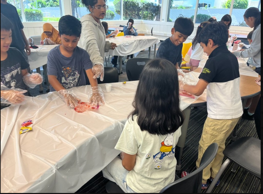 Elementary students and a SKITS volunteer performing a strawberry DNA extraction experiment at the Whitney STEM Camp